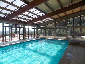 Una piscina interior con agua cristalina azul, ventanas amplias y techo de madera.