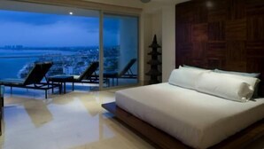 Um quarto com uma cama grande, vista da cidade através de janelas do chão ao teto, um ventilador de teto e uma parede de destaque em madeira.