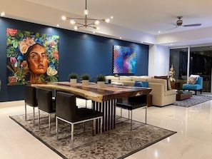Una sala de estar moderna con comedor, que incluye una mesa de comedor de madera, sillas negras, un sofá azul y un cuadro abstracto grande en la pared.