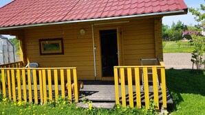 Une cabane en bois jaune avec un toit rouge, une véranda dotée de rampes jaunes et une porte donnant sur l’intérieur.