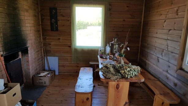 L’intérieur d’un chalet rustique, avec des murs en bois, une cheminée en briques, un banc en bois et une table sur laquelle est posé un vase rempli de fleurs séchées.