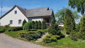 Une maison blanche dotée d’un porche, entourée d’un jardin où poussent différentes plantes et fleurs.