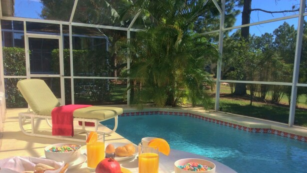 En frukostuppsättning vid poolen med en korg av rotting, frukt, flingor och en badanka i gummi.