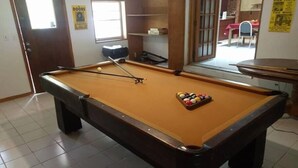 Une table de billard avec un queue et des billes, une porte, une fenêtre et une affiche accrochée au mur.