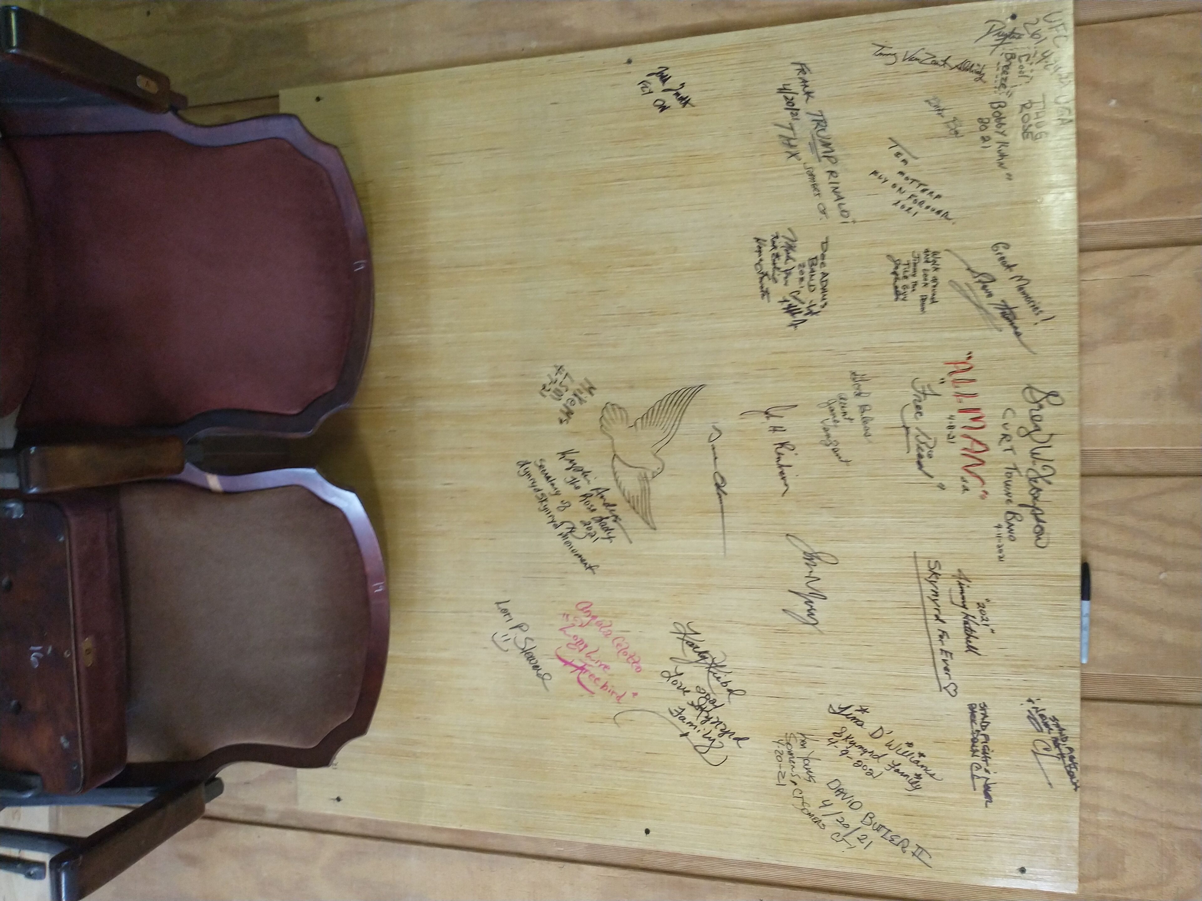 Een houten oppervlak met met de hand geschreven aantekeningen en handtekeningen, waarschijnlijk een gastenboek of inschrijfformulier, met een violencase gedeeltelijk zichtbaar aan de linkerkant.