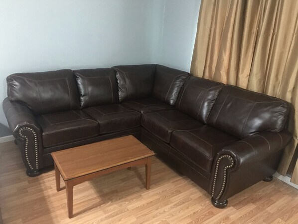 Ein braunes, ledernes Ecksofa mit einem Couchtisch aus Holz in einem Raum mit Holzboden und hellblauen Wänden.
