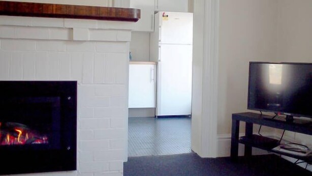 Una sala de estar con chimenea, televisión y una cocina al fondo.