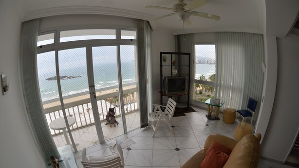 A living room with a large glass door leading to a balcony with a view of the ocean and beach.