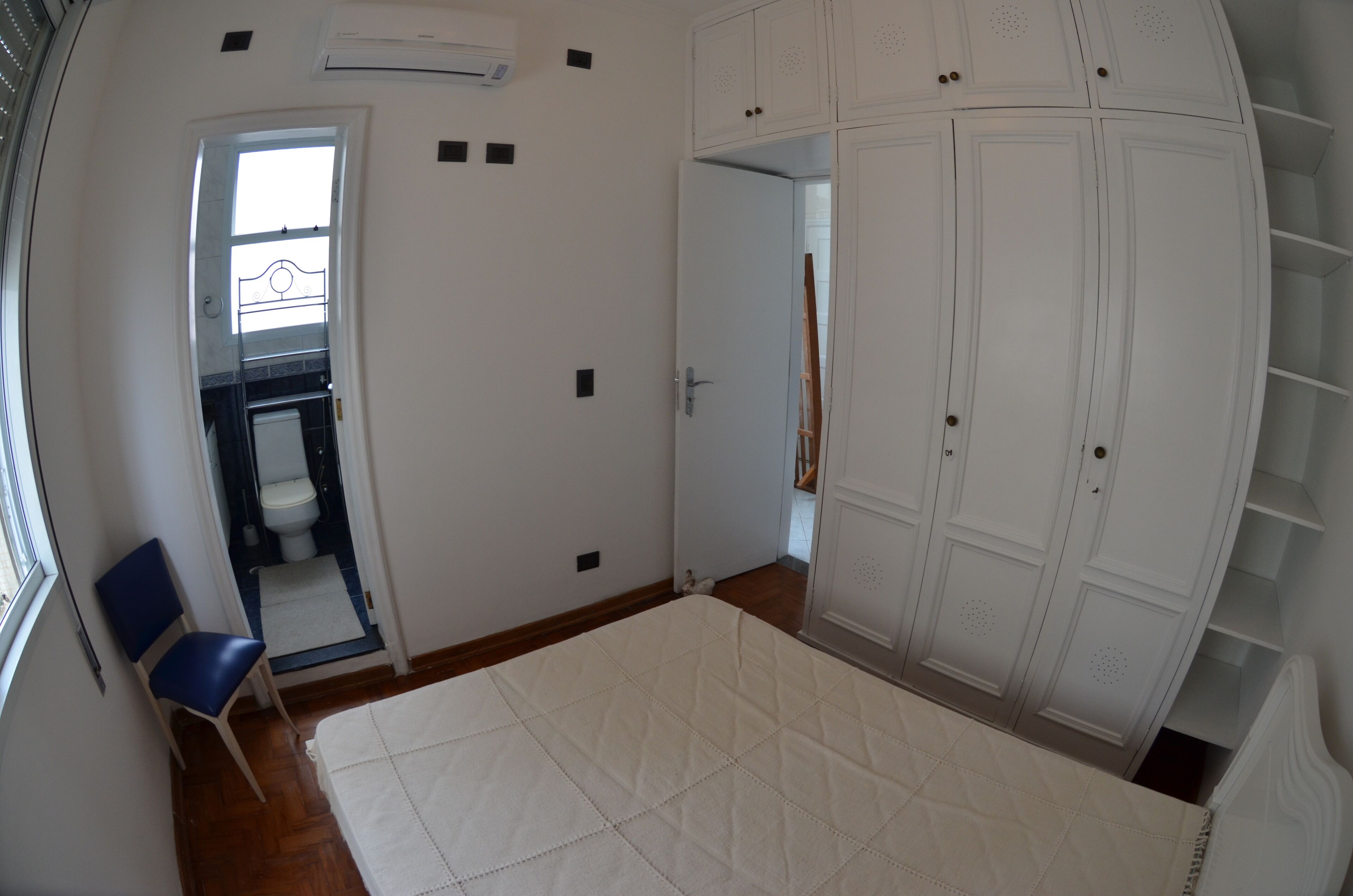Un dormitorio con una cama grande, un armario, una silla y un baño visible a través de una puerta abierta.