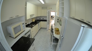 A compact kitchen with white cabinets, a microwave, a refrigerator, and a small dining area with a chair and table.