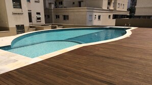A rooftop swimming pool with a wooden deck and a view of surrounding buildings.
