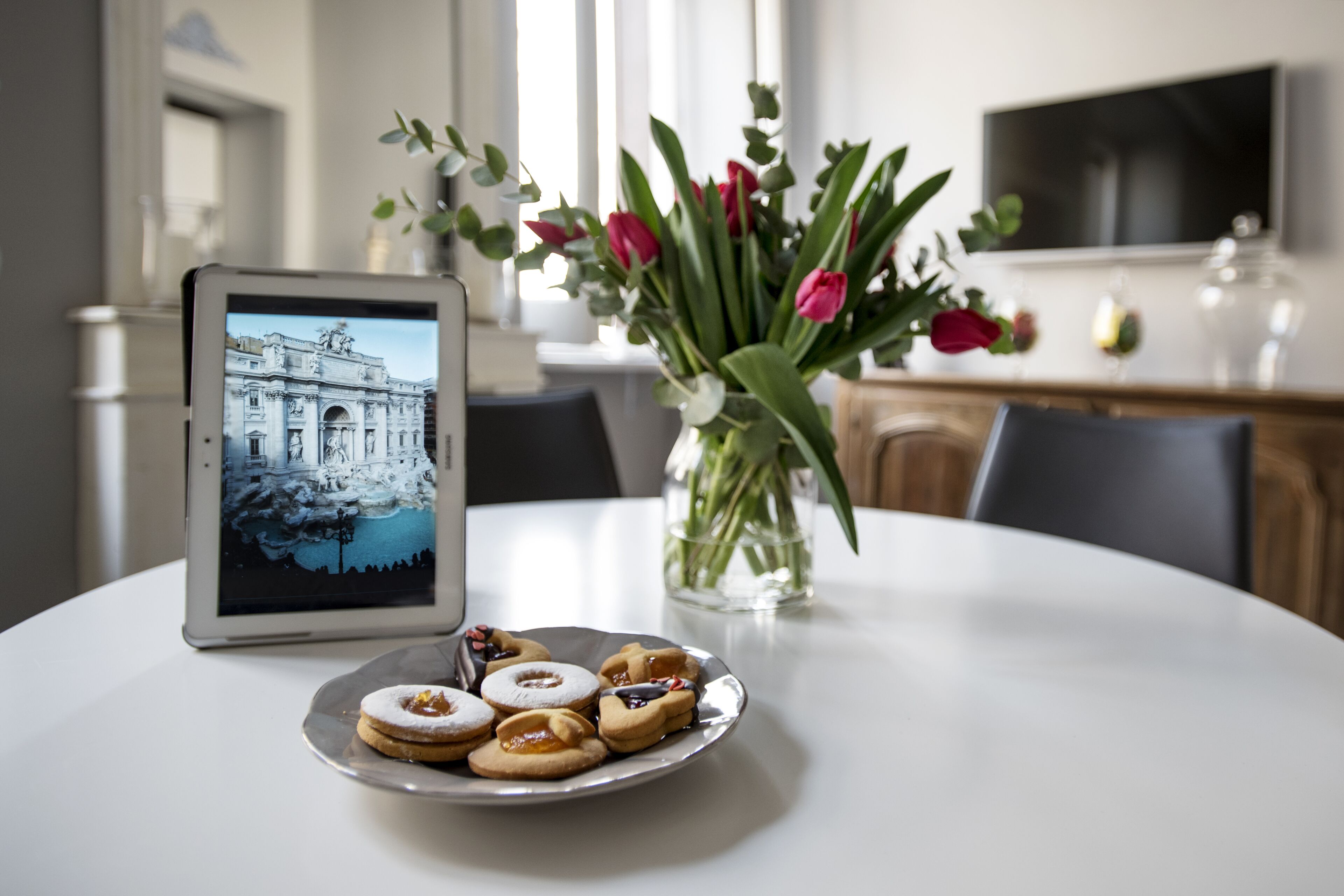Una mesa de comedor con un plato de galletas y una tableta que muestra una imagen de un edificio.