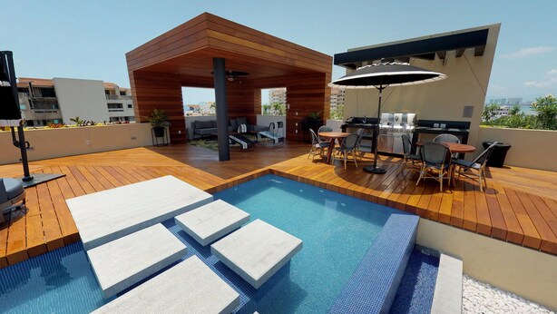 Un área de piscina en la azotea con terraza de madera, zona de estar cubierta y espacio para barbacoa.