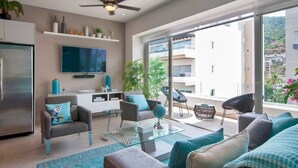 Una sala de estar moderna con un televisor de pantalla plana, asientos cómodos, una mesa de centro de vidrio y un balcón con vista a la ciudad.