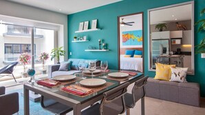 Un moderno salón con comedor, paredes color turquesa y un espejo grande que refleja la cocina.