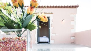 A clear glass vase with yellow flowers on a reflective surface, a tiled floor, and a building entrance with a door and a wall-mounted light.