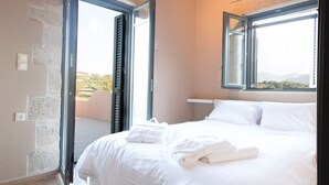 A bedroom with a wooden ceiling, an air conditioning unit, a bed with white linens, a window with shutters, and a view of the outdoors.