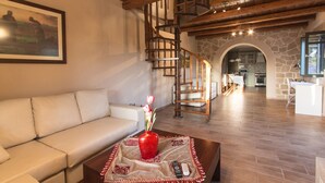 A spacious living area with a wooden staircase, a sofa, a coffee table with a vase, and a kitchen in the background.