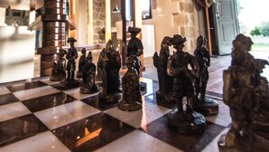 A chessboard with chess pieces in a room with wooden beams and stone walls.