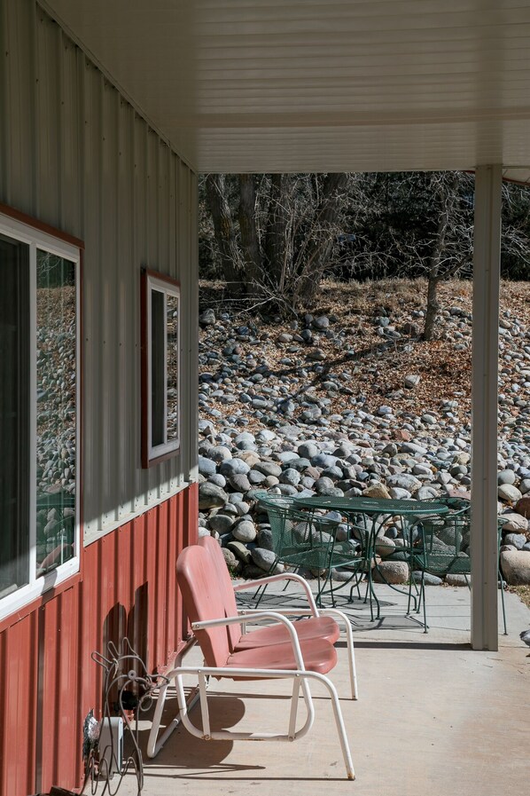 A covered patio with a red chair and a table, overlooking a rocky landscape with trees.