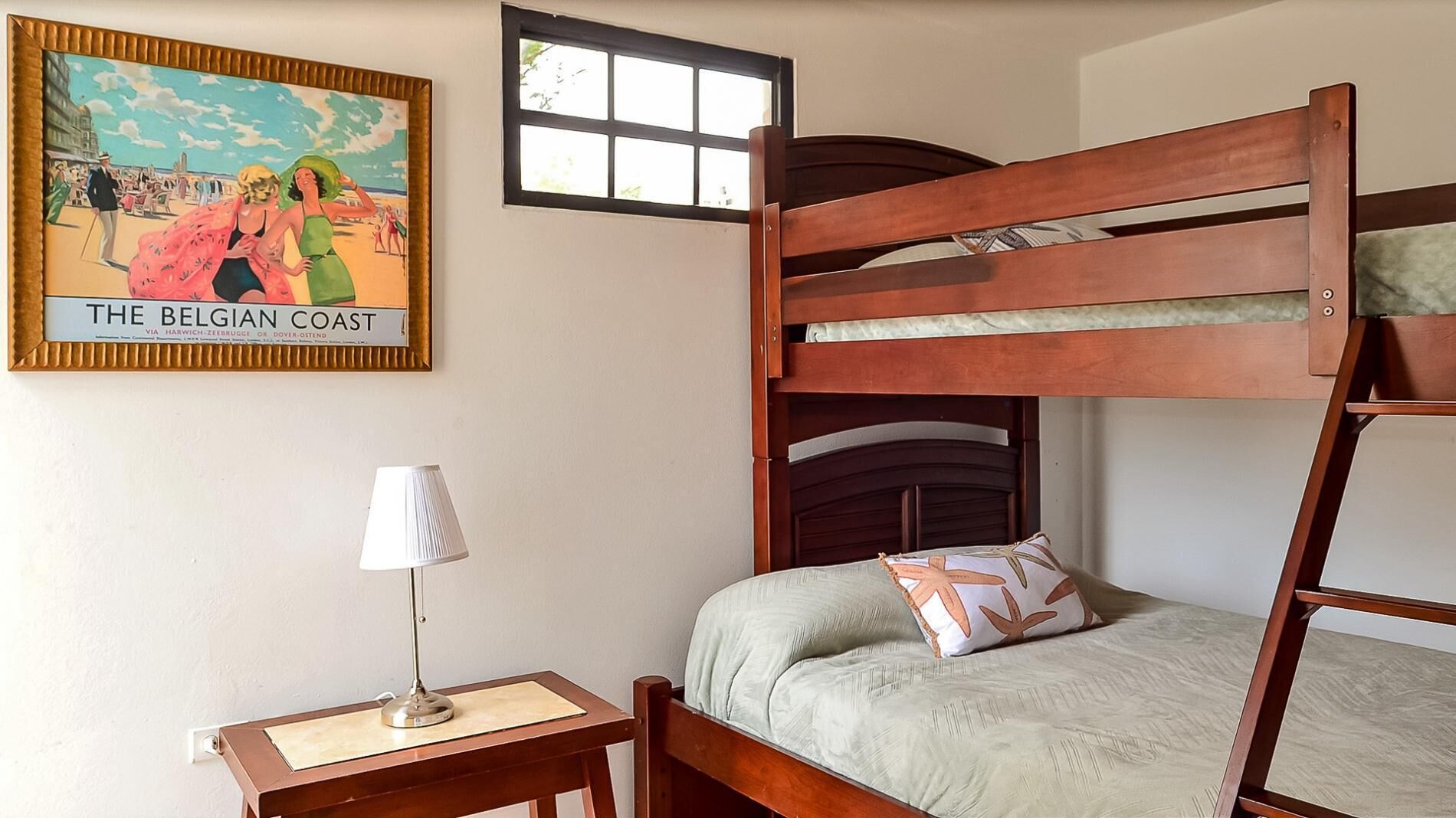 A bunk bed with a pillow, a bedside table with a lamp, and a framed picture on the wall.