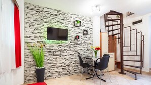 A modern living room with a stone wall, a flat-screen TV, a dining table with chairs, a red sofa, and a staircase. - Charming Duplex in the Heart of the Old Town (Split)