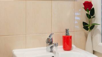 Un bagno con un lavandino bianco, un erogatore di sapone rosso e un vaso con una singola rosa rossa.