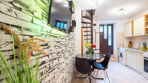 A modern kitchen with a stone wall, a dining area with a glass table, and a washing machine. - Charming Duplex in the Heart of the Old Town (Split)