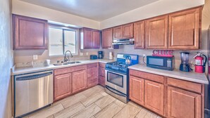 A kitchen with wooden cabinets, stainless steel appliances, a dishwasher, a stove, a microwave, a coffee maker, and a blender.