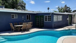 A swimming pool with a patio area, a table with chairs, and a building with a blue exterior.