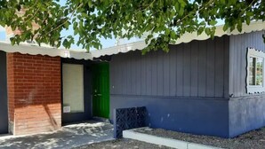 A small, single-story building with a brick wall and a green door.
