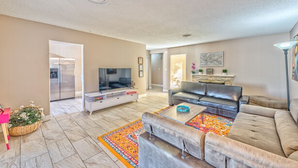 A spacious living room with a large flat-screen TV, a leather sofa, a coffee table, and a patterned rug.