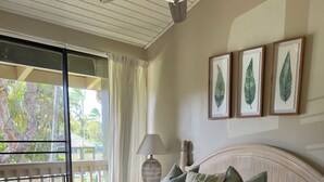 Ein Schlafzimmer mit einem Bett, einem Deckenventilator, einem Fenster mit Vorhängen und gerahmten Blattform-Kunstwerken an der Wand.