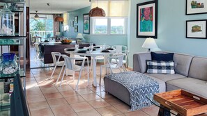 A spacious living area with a dining table, white chairs, a sofa, and a coffee table.