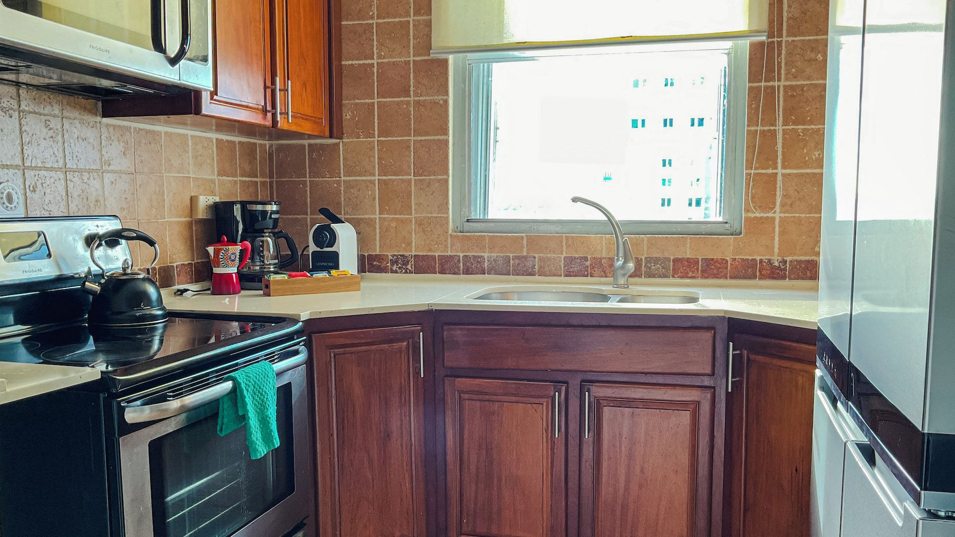 A kitchen with a stove, oven, coffee maker, and a window with a view of buildings.