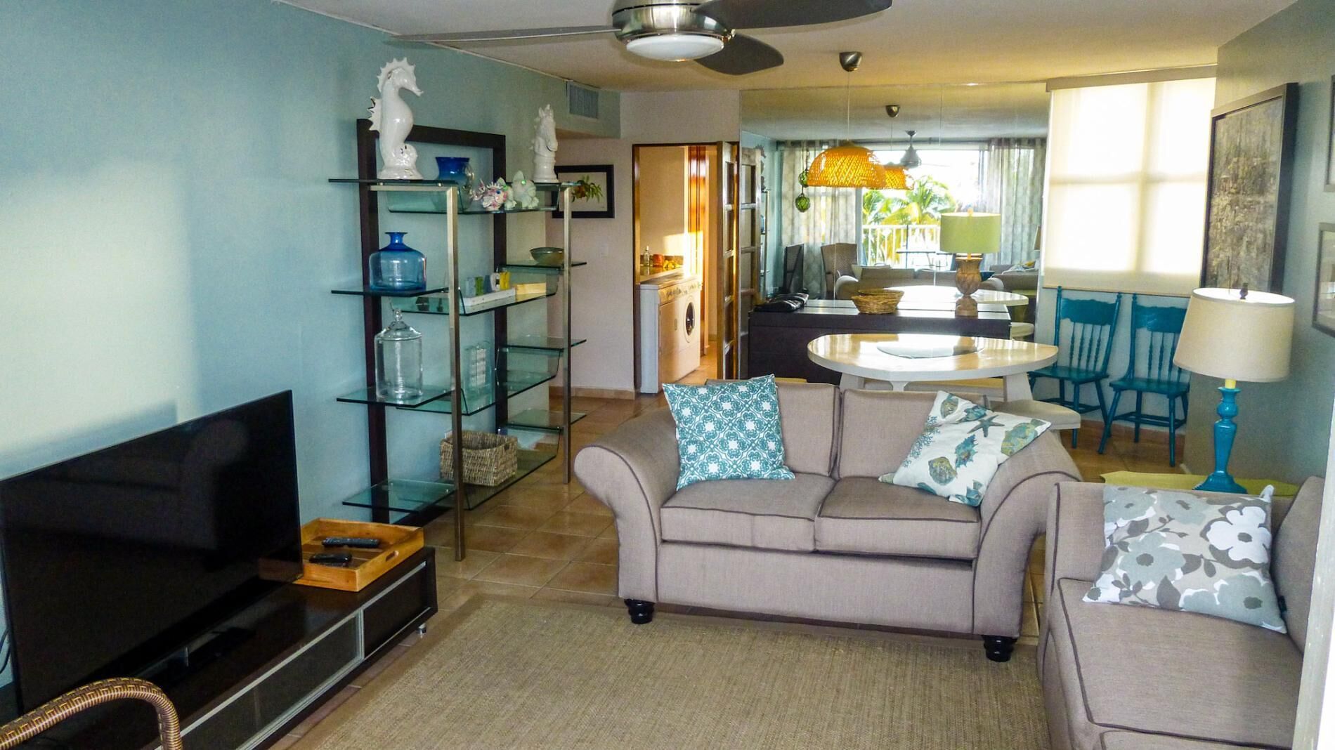 A living room with a sofa, TV, and glass shelves. There is a dining area with chairs and a table.