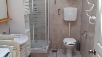 A compact bathroom with a shower, toilet, sink, and a washing machine.