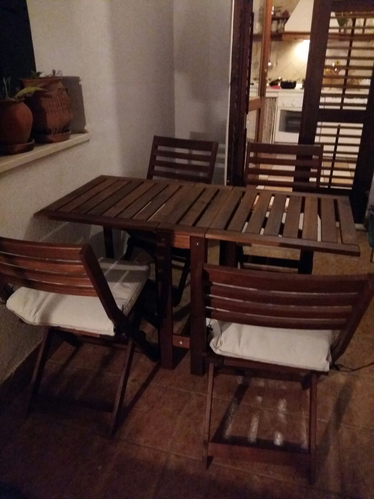A wooden dining table with four chairs, each with a white cushion.