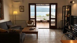 Un salon avec un canapé, une table basse et un téléviseur. On peut admirer la mer à travers une porte vitrée.