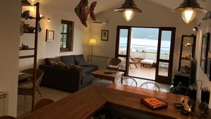 Un salon chaleureux avec un canapé, une table en bois et une vue sur la mer, visible à travers une porte vitrée.