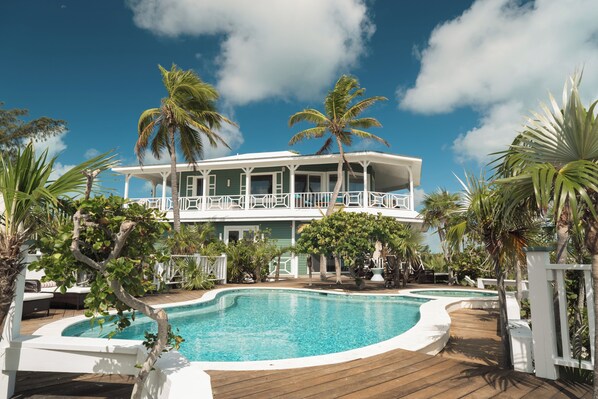 A two-story house with a pool, surrounded by palm trees and a wooden deck.