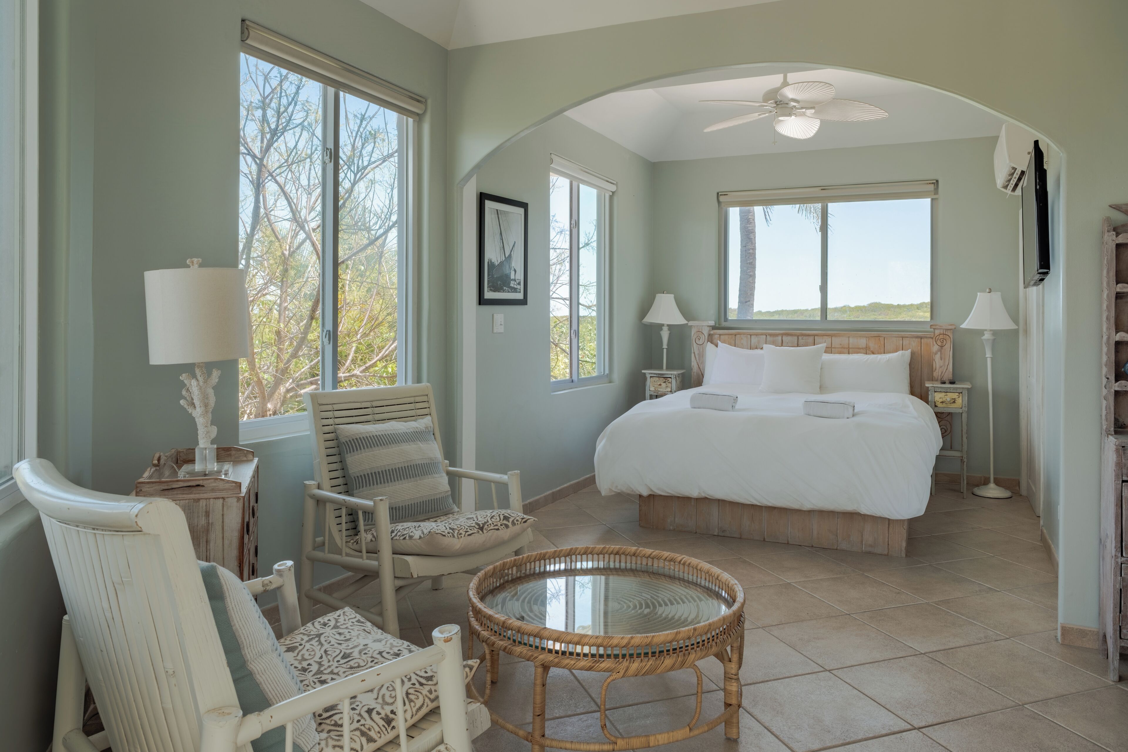 A bedroom with a large bed, a chair, a table, and a ceiling fan.