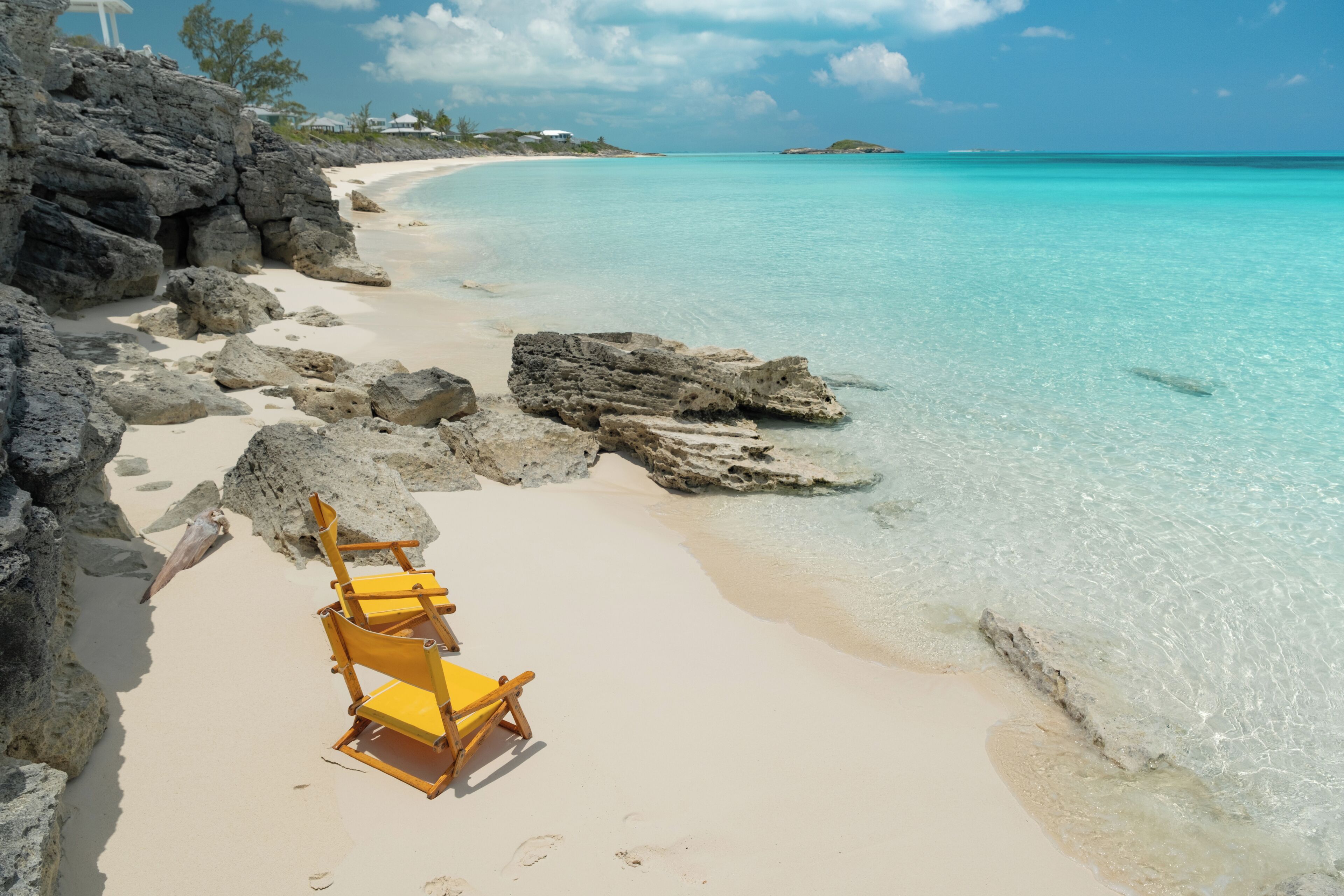 A beach with clear turquoise water, a sandy shore, and a yellow beach chair.