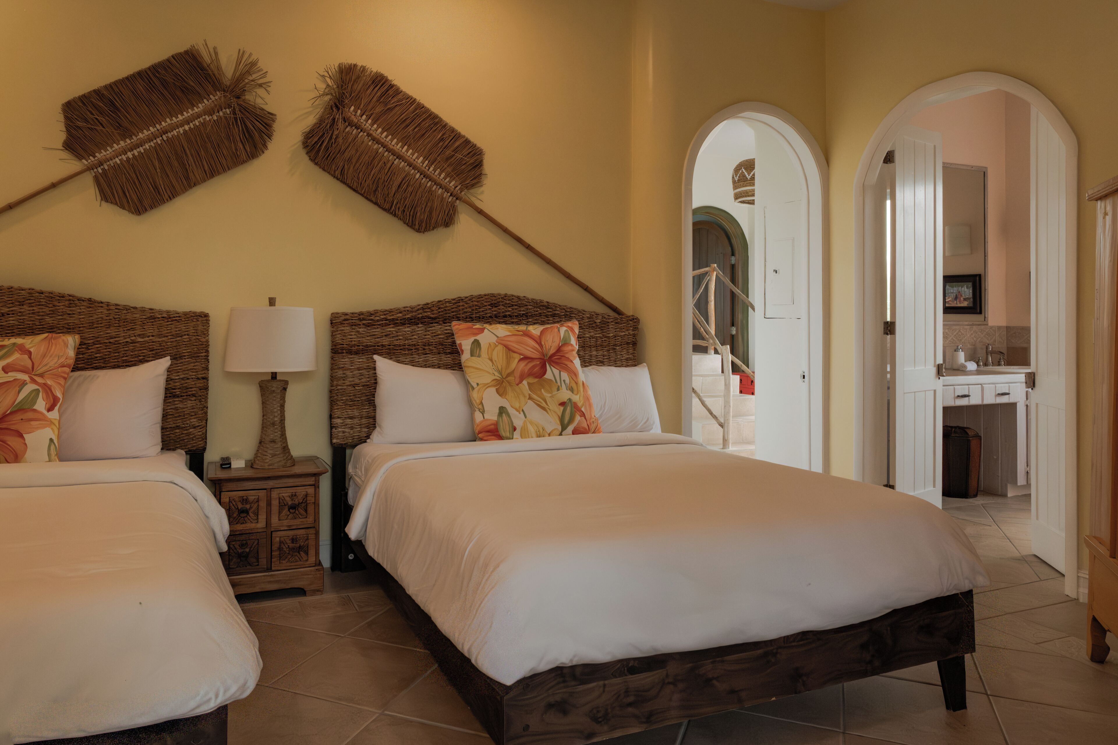 A bedroom with two beds, a nightstand with a lamp, and a bathroom visible through an archway.