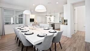 A modern kitchen with white cabinets, a dining area with a white table set for six, and a large window with blinds. - Sonoma Resort affordable 7bd home with pool (1849) (Kissimmee)