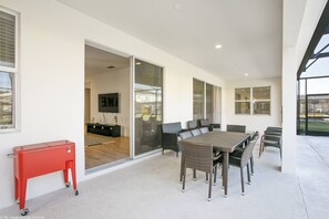 A covered patio area with a dining table and chairs, a red cart, and a sliding glass door leading to an interior space.