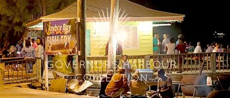 A waterfront food stall with a sign reading "Anchor Bay Fishery" and a collection of people gathered around.