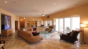 A spacious living room with a large sofa, a glass coffee table, and a dark wicker chair. There is a television on the left and a large window on the right. - Luxury Oceanfront Villa in Cabo San Lucas (Cabo San Lucas)