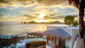 A coastal resort with a pool, thatched-roof structures, and a view of the sea at sunset. - Luxury Oceanfront Villa in Cabo San Lucas (Cabo San Lucas)