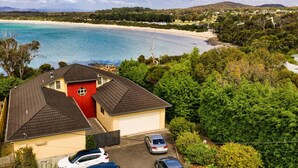 A coastal property with a red house, a garage, and a driveway with parked cars. - Beachfront Retreat with Direct Beach Access | Family Friendly (Greens Beach)